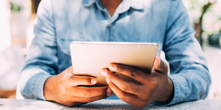 A man in a semi casual blue jean shirt working on his tablet.