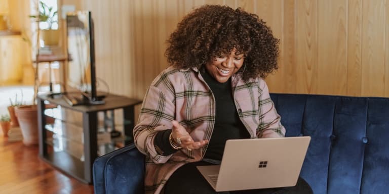 A young woman sitting on a blue velvet couch using the Smart Solutions tool on her laptop to view her benefits and profile.