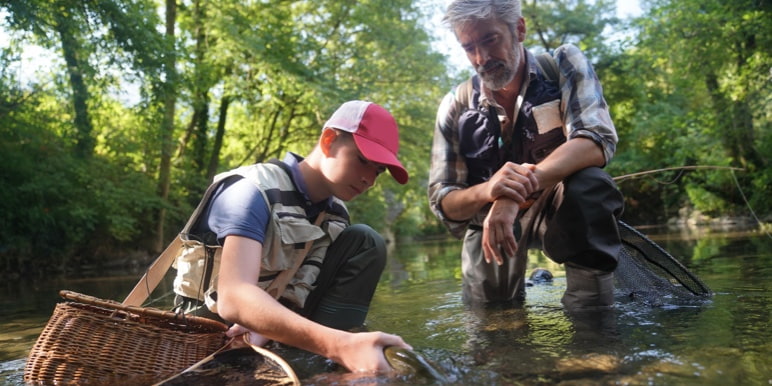 A retired man guiding his grandson while he catches a fish in the river.