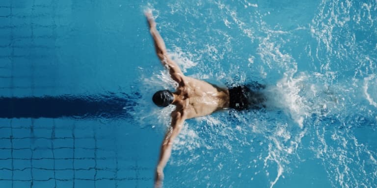 A man swimming at his maximum performance in an Olympic-sized swimming pool during a competitive race. 