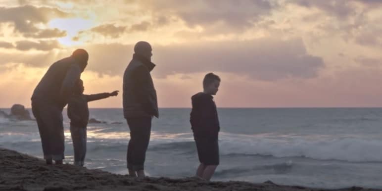 Two fathers and their son's standing on the beach.