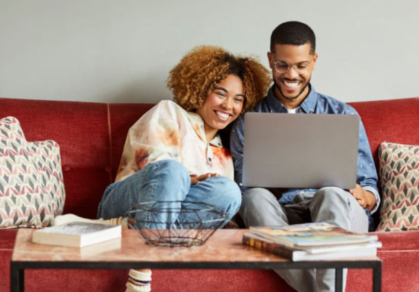 A happy young couple on a laptop, sitting on the couch in their new home. 