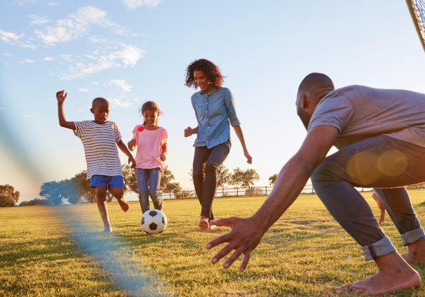 A healthy young couple playing soccer with their two children outside.