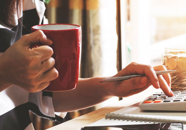 A young man with coffee in hand, submitting his tax returns on his computer. 