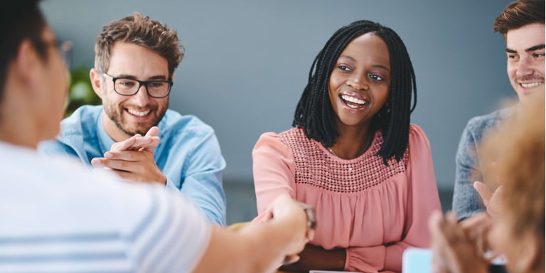 Colleagues seated around a table clapping for a fellow worker who is receiving a handshake for good work.