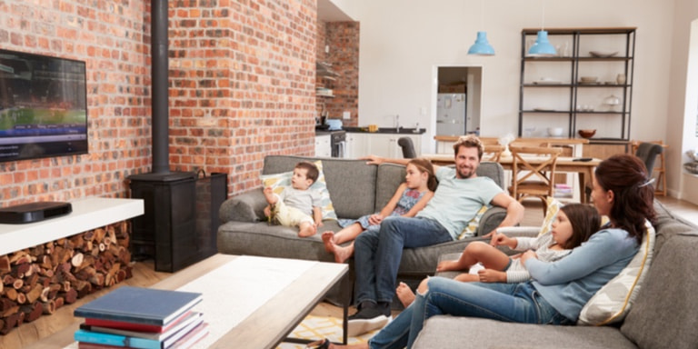 A family of five sitting on their couch in the lounge watching TV.