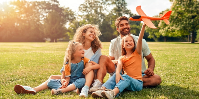 Happy married couple with their two young daughters enjoying quality time outdoors, confident that their legacy has been secured for their chosen beneficiaries