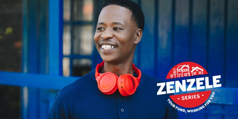 Smiling young man wearing red headphones around his neck, standing in front of a blue wall.