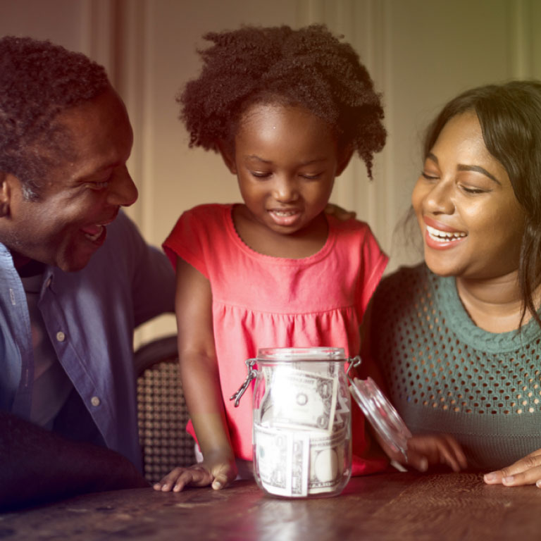 A couple and their daughter putting money into a jar.
