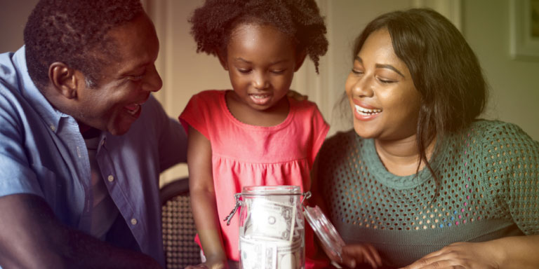 A couple and their daughter putting money into a jar.
